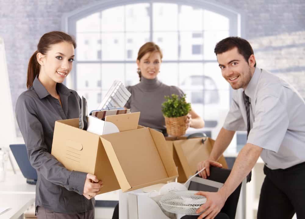 Young office workers moving office, unpacking boxes, smiling.