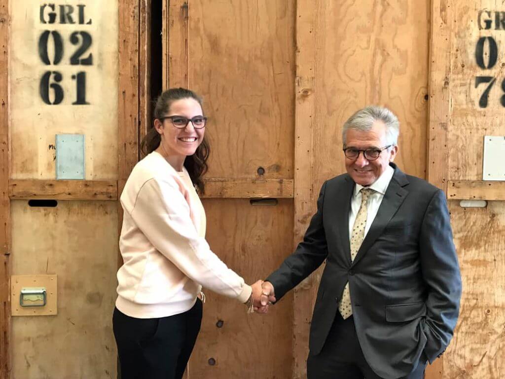 Man In Suit Shaking Hands With Young Woman In Front Of Crates