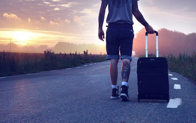 A man walking down a road with a suitcase at dawn.