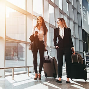 Two business women walking through an airport with luggage