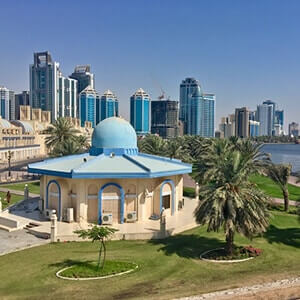View of a beautiful Mosque surrounded by trees and overlooked by tall office buildings in Sharjah, UAE