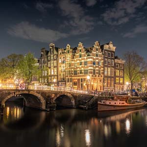 A nighttime shot across an Amsterdam canal picturing a lit bridge and elegant building