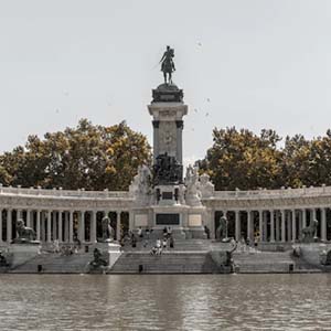 A shot of the El Retiro statue in Madrid, with trees behind the white-walled structure