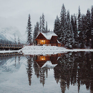 Snowy cabin on a lake scene against a backdrop of Candian mountains