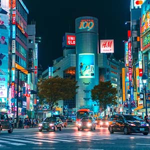 A busy square full of cars and people under a wall of lit screens in Shibuya, Japan