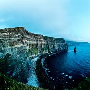 A landscape view of a white cliff face overlooking a rounded cove with a dark sea