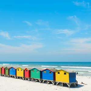 A row of colourful beach huts sitting on a sandy beach with a clear sky and blue waters