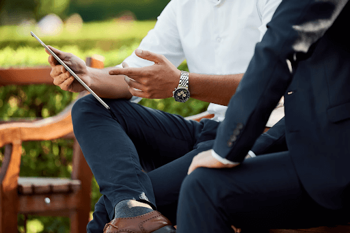 Smartly dressed business men sitting on a bench outside having a meeting and holding a tablet