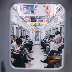 Through a window into a subway car in Japan with passengers sitting and looking at their phones