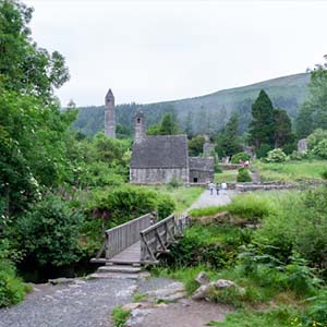 View of an old monastery over a small wooden bridge surrounded by green fields, trees and hills in Ireland