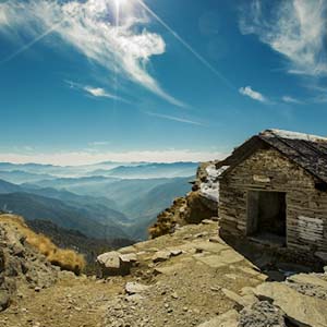 A slate house on rocky ground overlooking mountain ranges in India