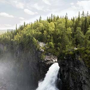 A waterfall in Gäddede, Sweden pouring from a rocky mountain covered in tall trees