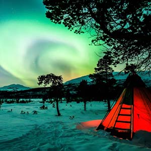 Red tent in a snow covered field in Sweden with the Northern Lights bright overhead