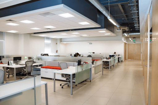 An office with desks, chairs and 1 employee sat working on a computer.