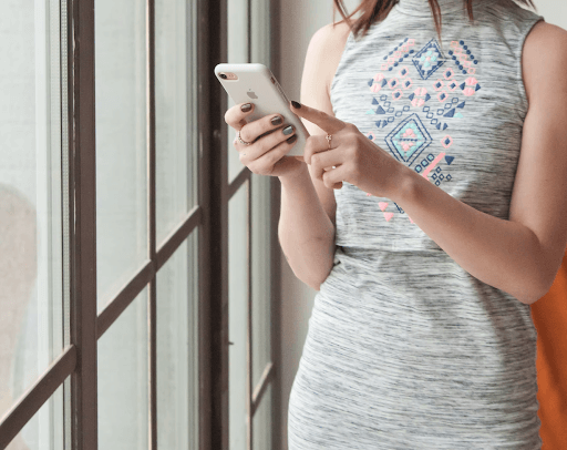 Woman holding a smartphone in front of a window.