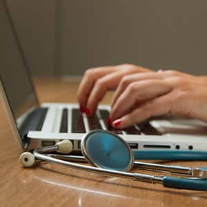 healthcare professional using a laptop with a stethoscope beside the keyboard