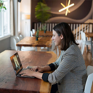 Woman sitting at a wooden table in an office attending a conference call on her laptop