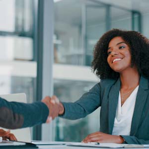 Two smartly dressed people shaking hands and smiling in an office