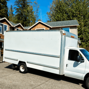 A white moving van in the driveway of a large house in the USA with blue skies
