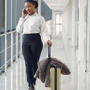 A woman wearing a work uniform walking through an airport with a small suitcase