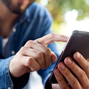 Man sitting at a coffee table with a white cup scrolling on his phone