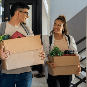 Two people holding boxes of belongings and walking along a corridor