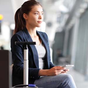 Woman in a work blazer sitting beside her suitcase in an airport terminal