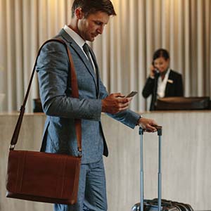 Man wearing a suit and wheeling a suitcase in a hotel lobby