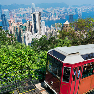 Red Peak Tram heading up a hill in Hong Kong with the view of skyscrapers behind