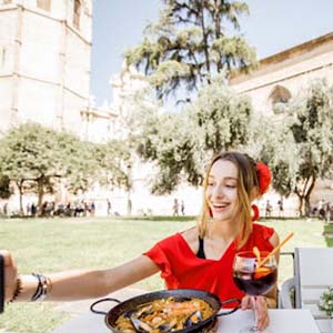 A young woman enjoying Spanish paella and red wine sitting outdoors in Valencia, Spain