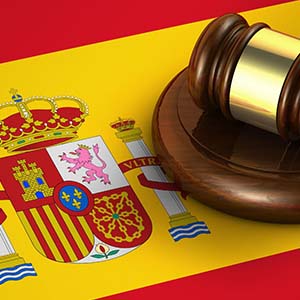 A courtroom gavel and mallet upon a Spanish flag